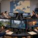 Studio européen de développement de jeux vidéo avec écrans de travail, graphiques financiers abstraits et carte non légendée de l’Europe dans une ambiance technologique sobre.